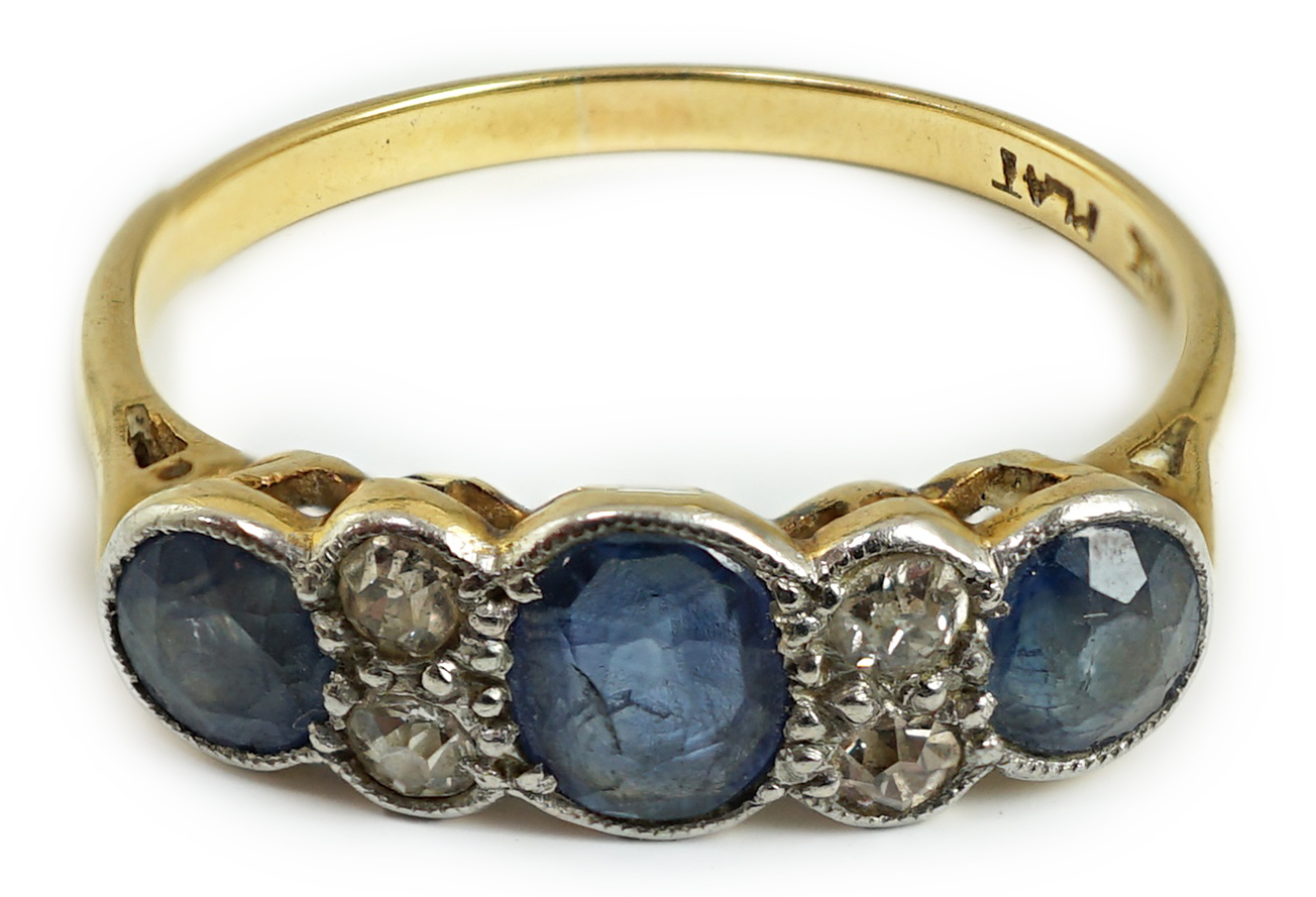 A 1920's 18ct gold and platinum, millegrain set three stone sapphire and four stone diamond half hoop ring